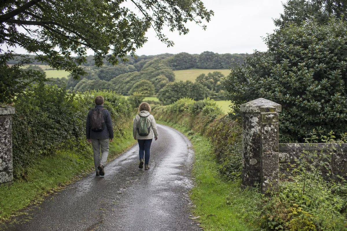 Two walkers following a damp hedge-lined lane through rolling countryside